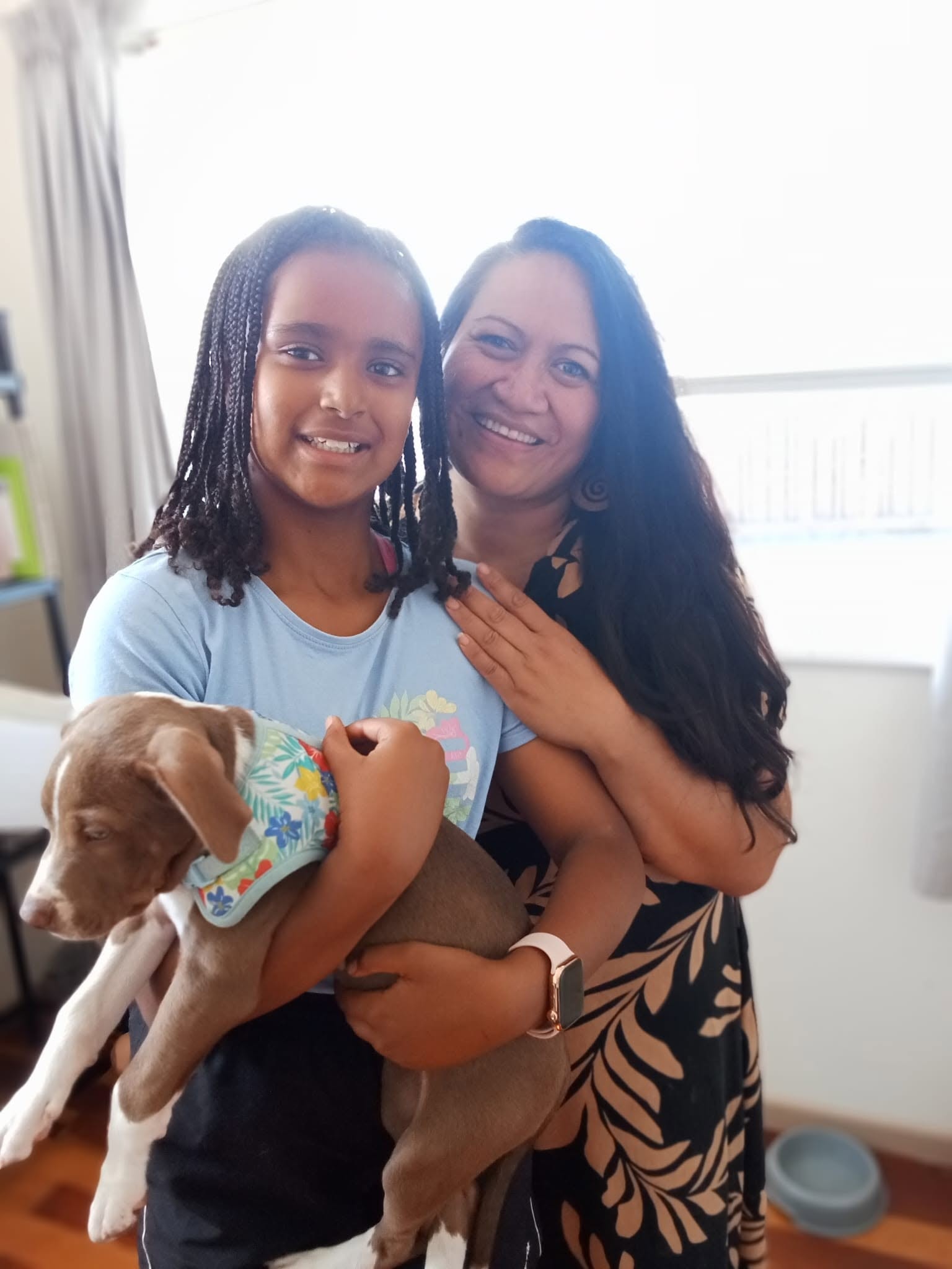 A mother and daughter smiling while holding a foster puppy